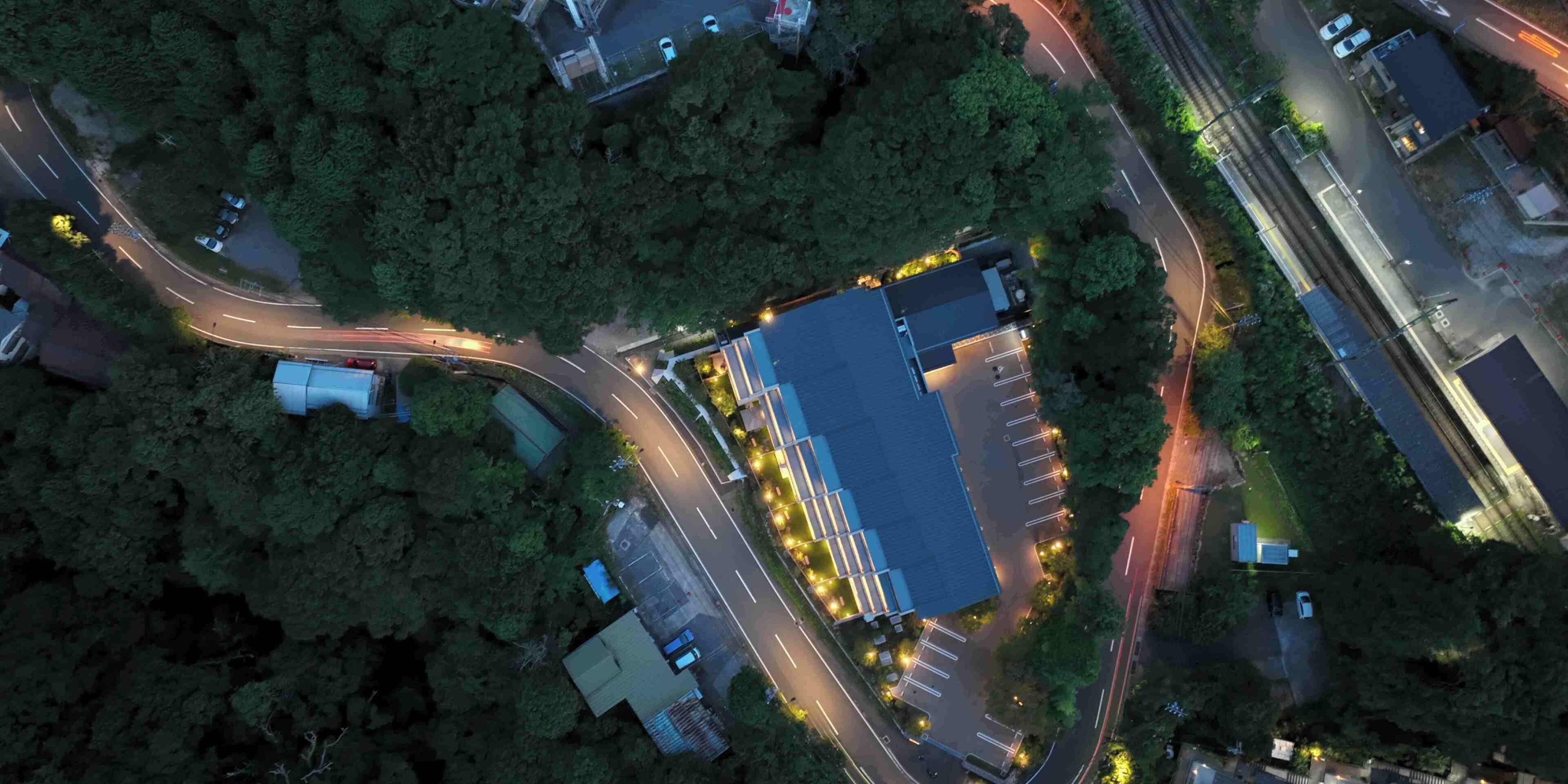 An aerial view of a parking lot with a large building, surrounded by trees and connected by roads.
