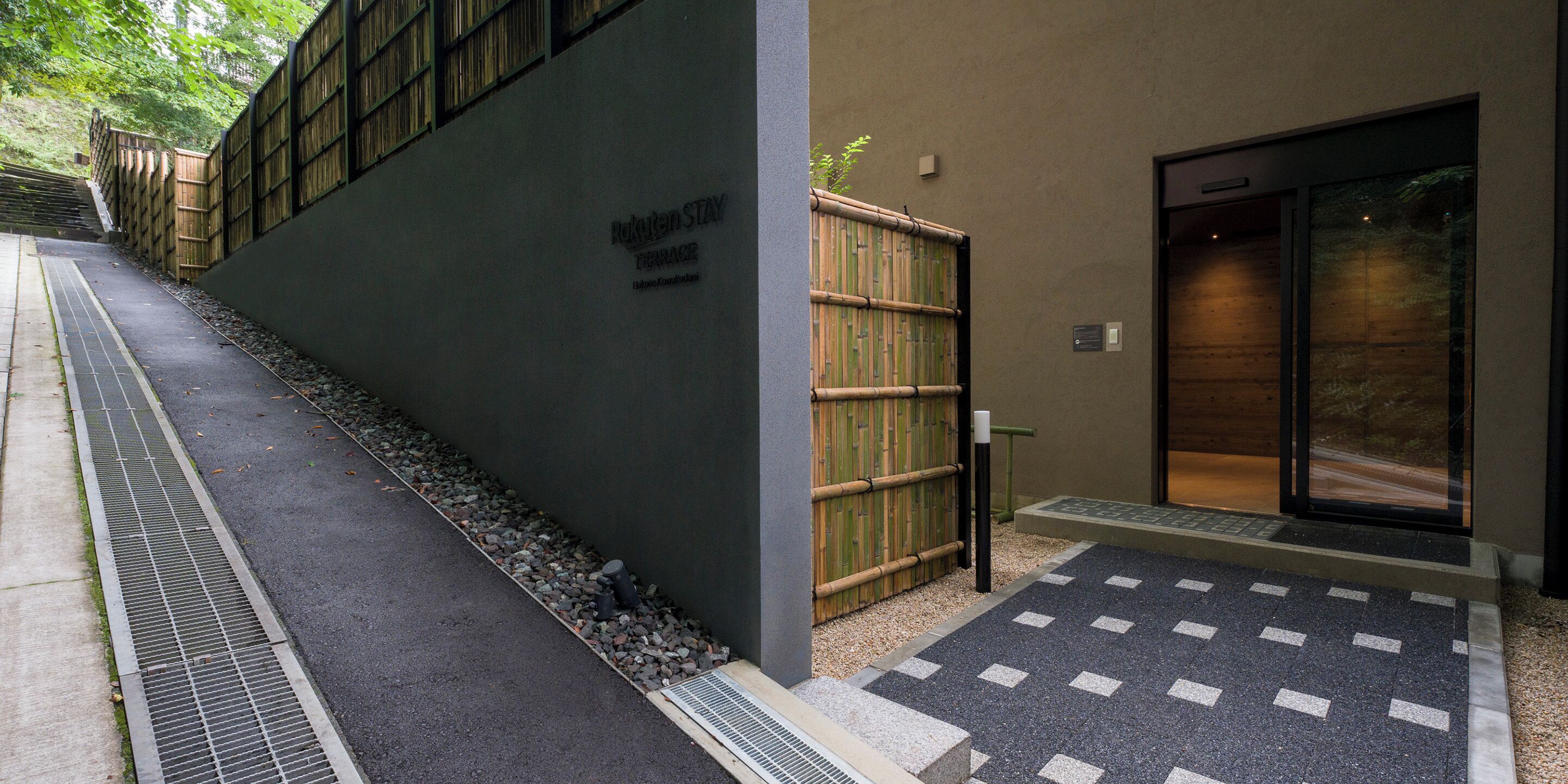 A building entrance with a bamboo fence, a sign reading "Hotel Stay," and a tiled entrance area.