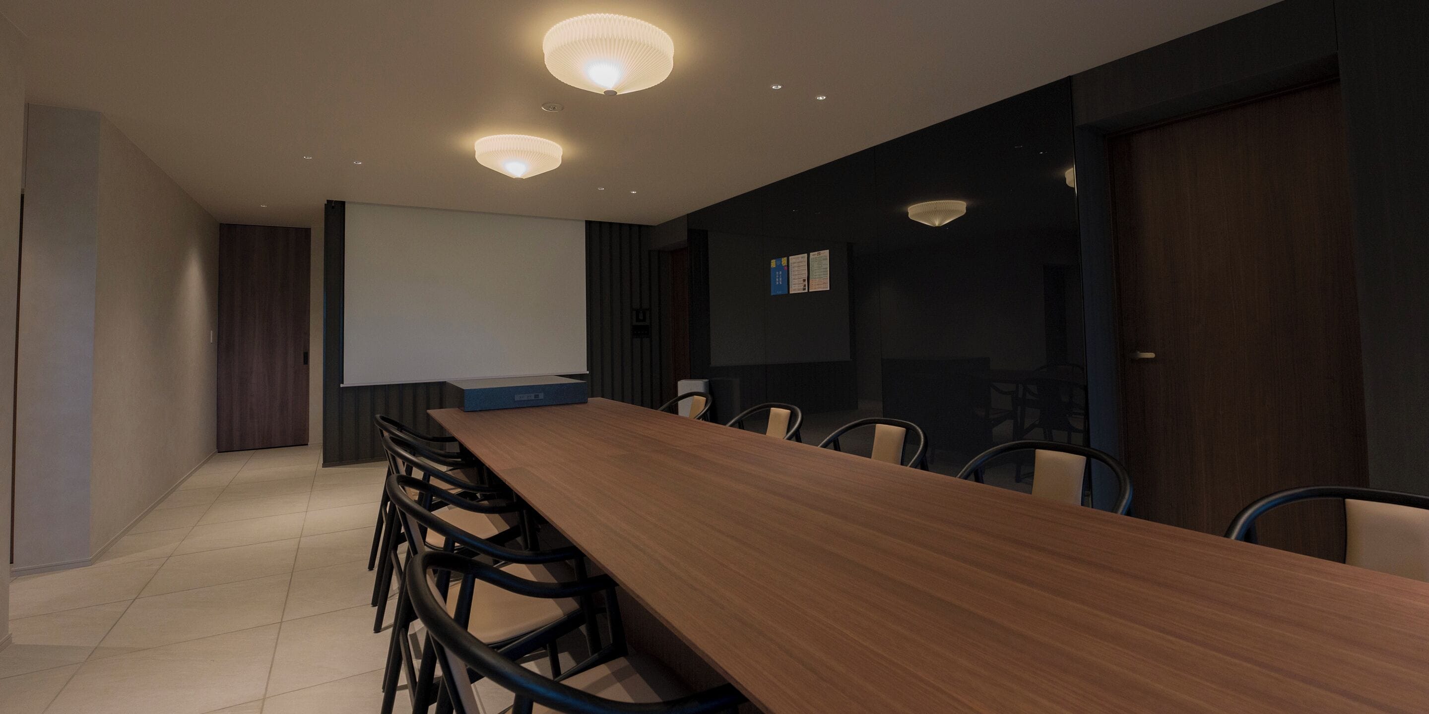 A conference room with a long wooden table, black chairs, and recessed ceiling lights.