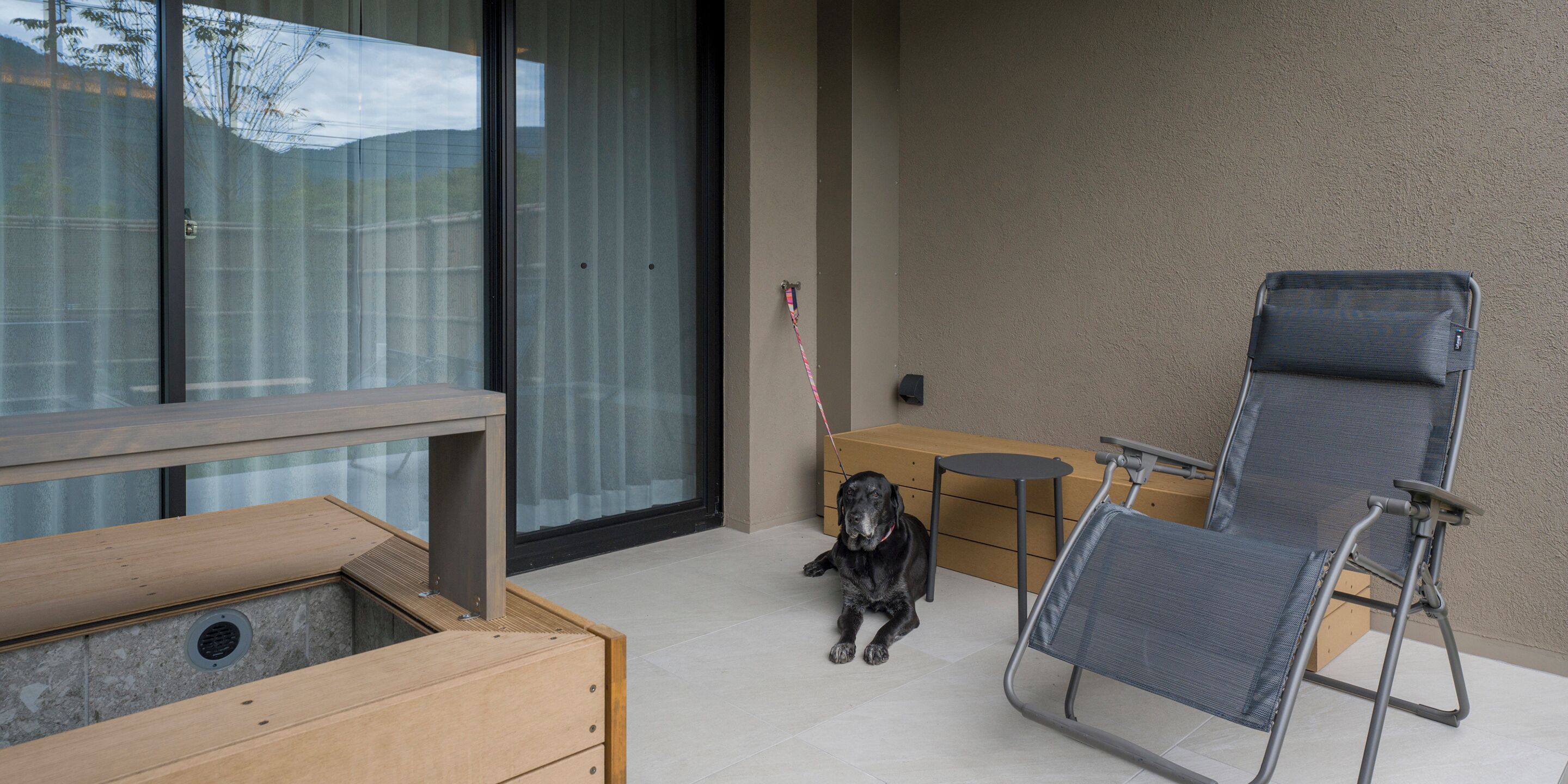 A patio area with a dog, a folding chair, and a wooden bench.