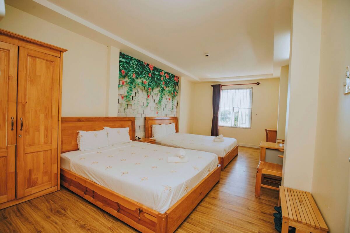 A hotel room with two wooden beds, a wardrobe, a bench, and a decorative wall.