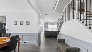 Un salon moderne avec une table à manger en bois, un canapé et un escalier doté d’une rampe noire.