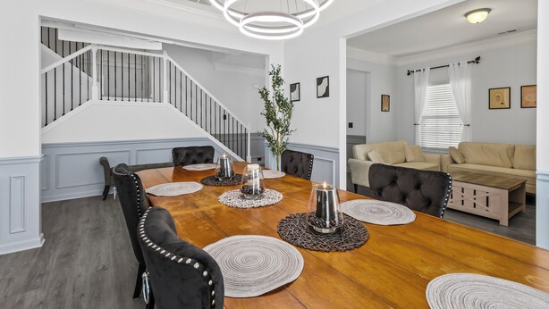 Un coin repas avec une table en bois, des chaises à revêtement noir et un escalier en arrière-plan.