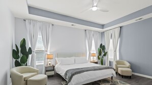 Une chambre à coucher comprenant un lit, deux tables de chevet, un ventilateur de plafond et une chaise.