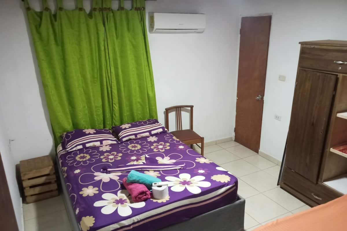 Une chambre à coucher avec un lit, des rideaux verts, un climatiseur, une armoire en bois et une chaise.