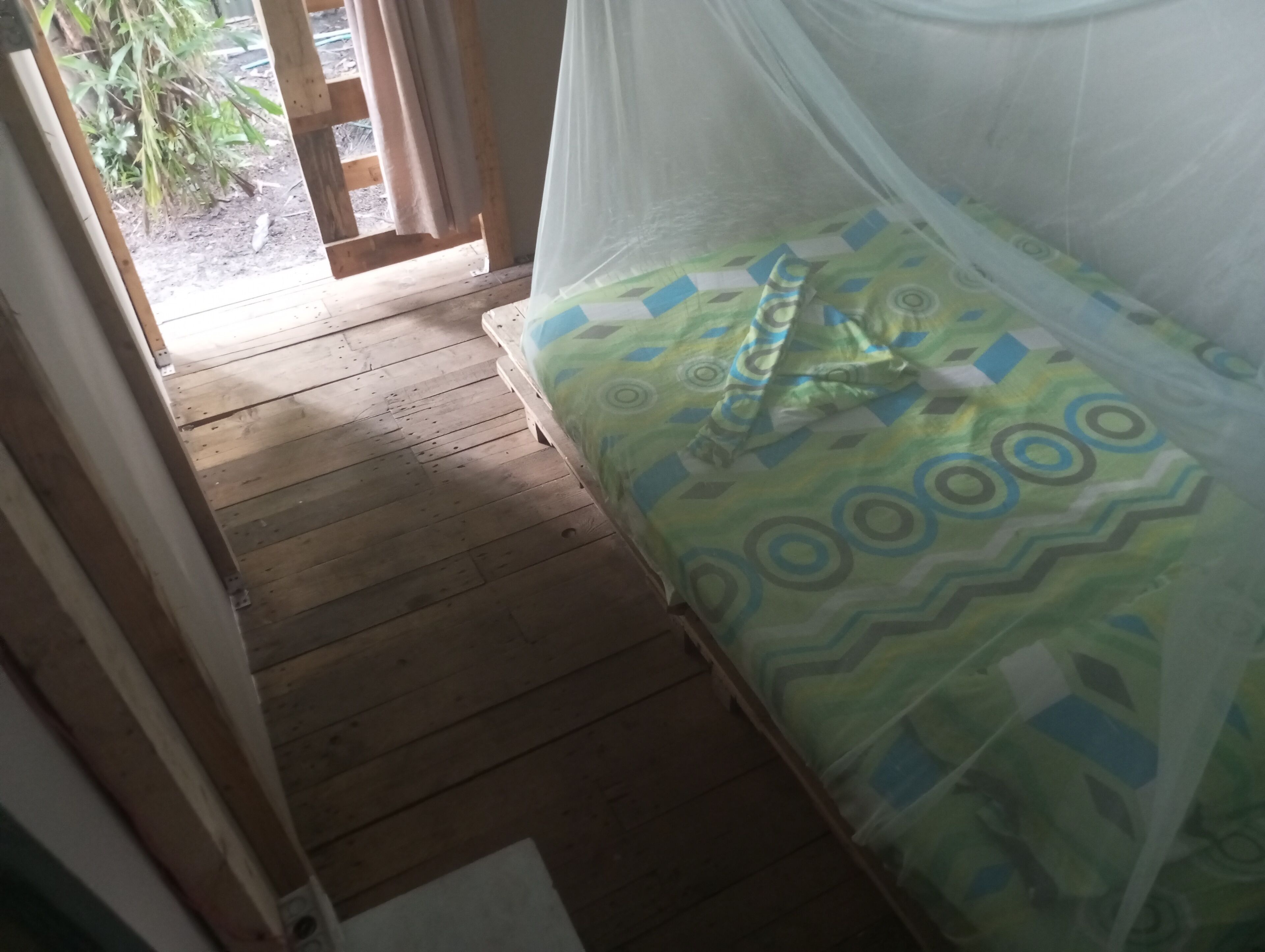 A wooden floor leading to a bed with a green and blue patterned bedspread and a mosquito net.
