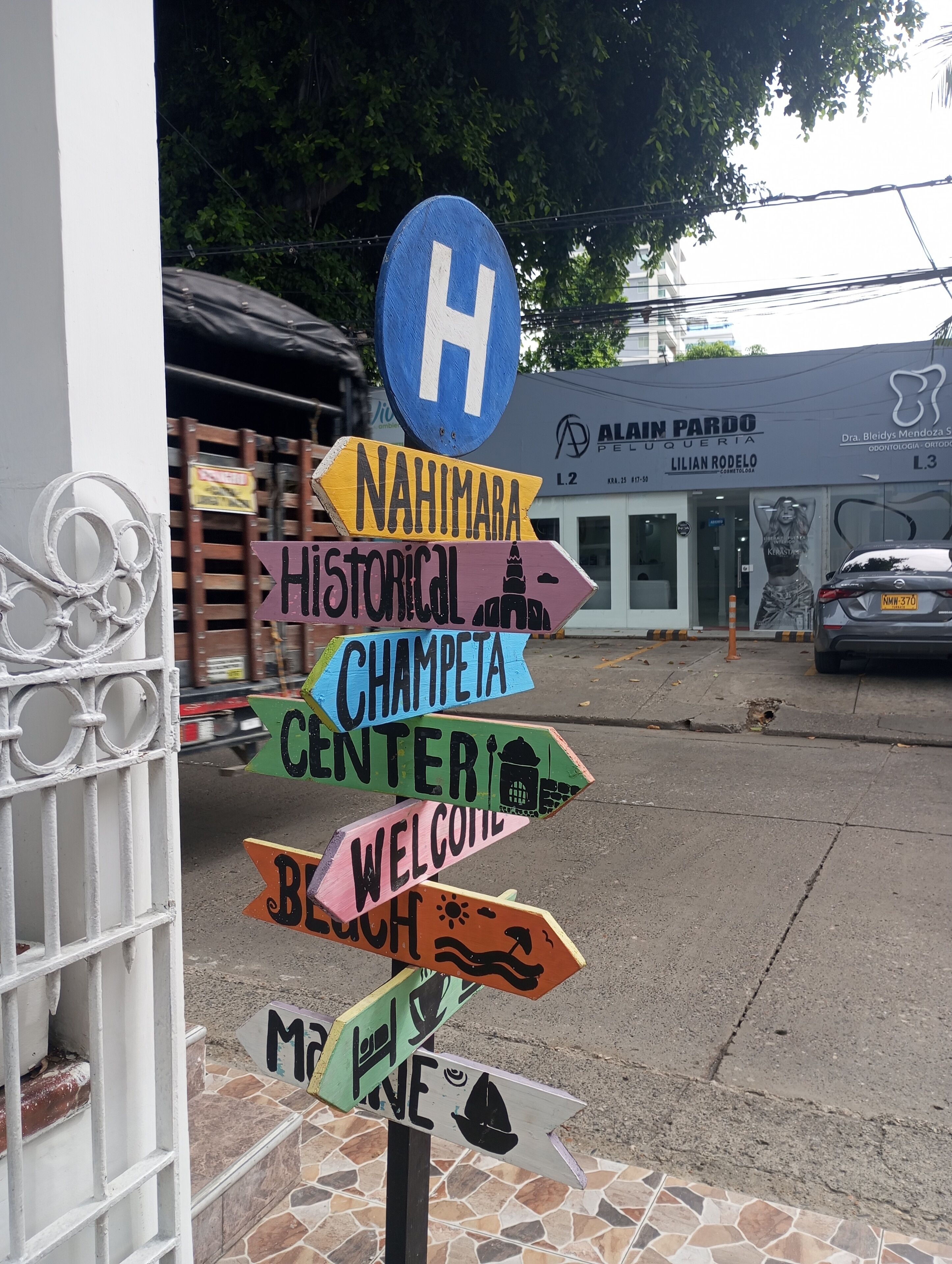 A colorful signpost with various directions and a blue 'H' sign above it.