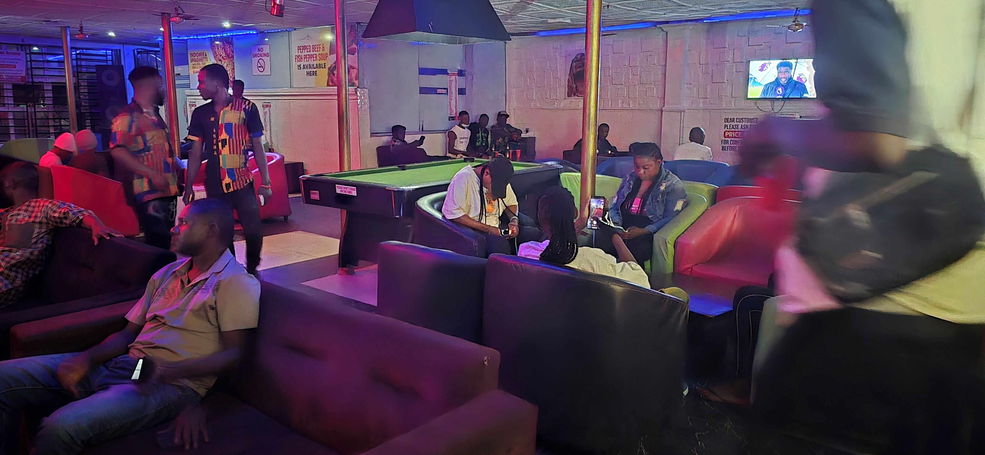 A billiards room with pool tables, seating areas, and a television screen.