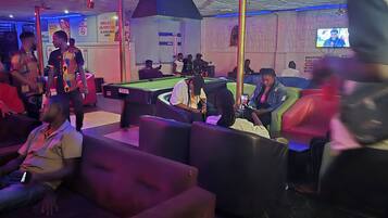 A billiards room with pool tables, seating areas, and a television screen.