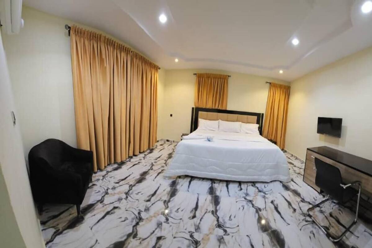 A hotel room with a bed, a desk, a chair, and curtains.