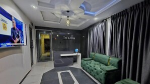 A modern living room with a green sofa set, a flat-screen TV mounted on the wall, and a reception desk labeled "Tm Arena".