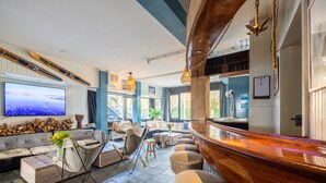 A bar area with a wooden counter and stools, a television mounted on the wall, and a seating area with sofas and chairs.