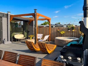 An outdoor patio with a barbecue grill, wooden lounge chairs, a hot tub, and a pergola structure. - Accommodation by the water with sauna + hot tub (Kaag)