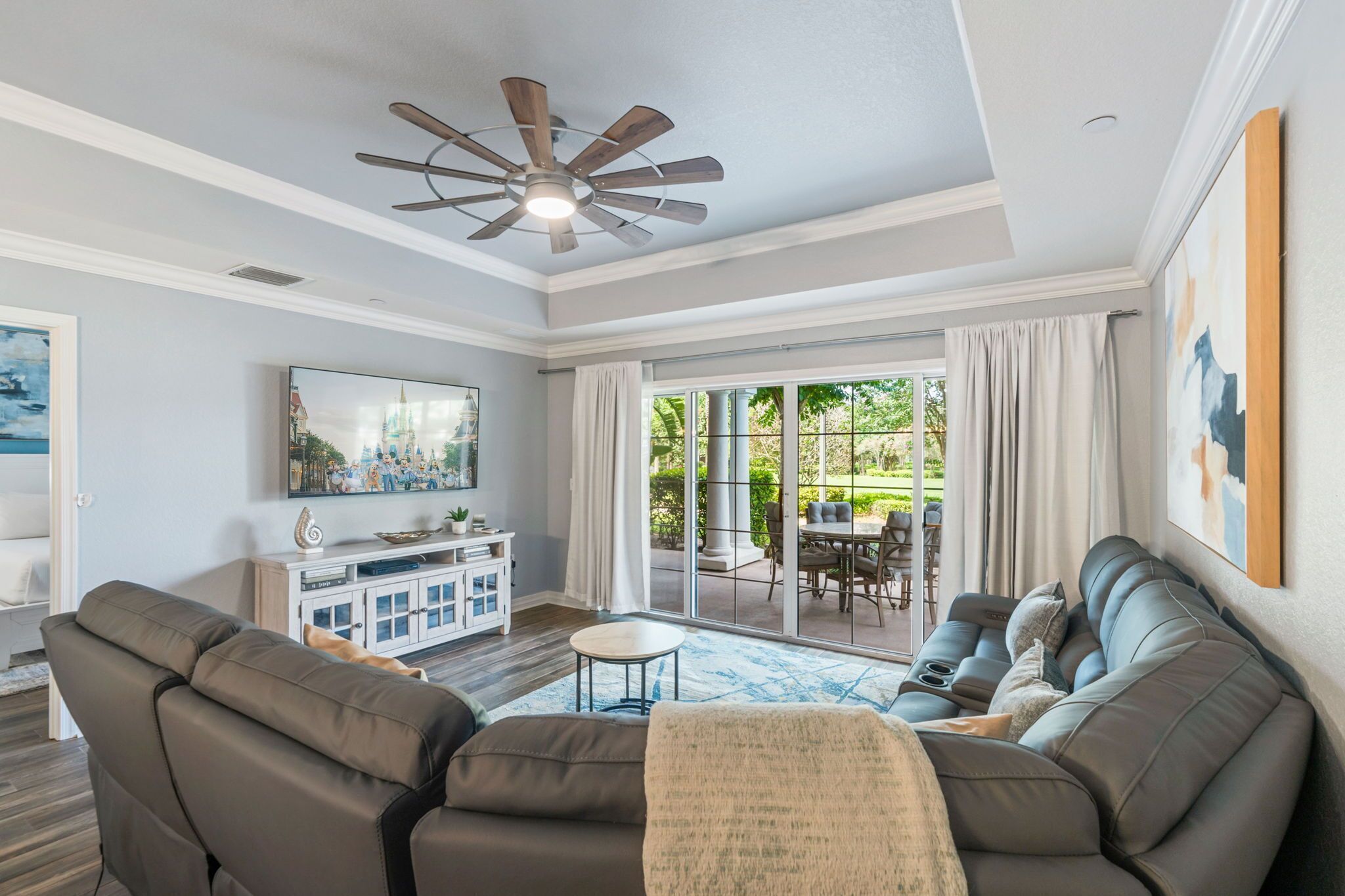 A spacious living room with a large gray sectional sofa, a ceiling fan, and a dining area visible through glass doors.