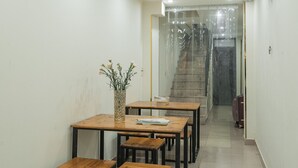 A hallway with a staircase, wooden tables, and chairs, and a wall-mounted fan. - Laura house (Hanoi)
