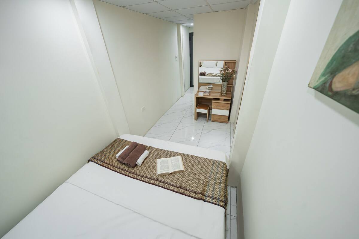 A narrow hotel room with a bed, a small desk, and a mirror.