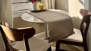 Une pièce avec une table ronde, deux chaises, un vase de fleurs, un miroir et une vue sur un balcon doté d’une balustrade.