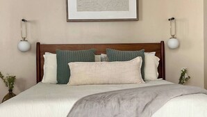 Un lit bien fait, avec une tête de lit en bois, deux lampes de chevet et une œuvre d’art abstraite encadrée accrochée au mur.