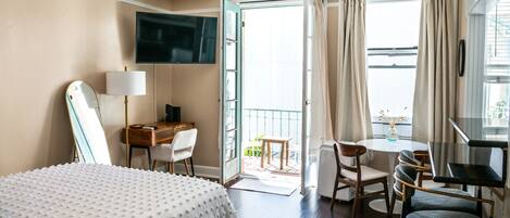 A hotel room with a bed, desk, chair, and a balcony with a table and chairs.