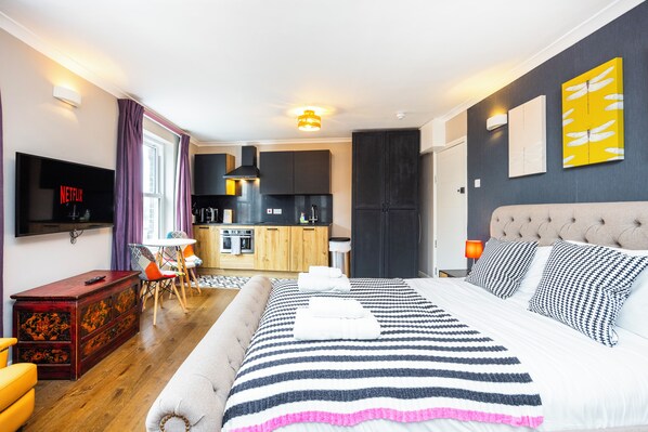 Una habitación de hotel moderna con una cama grande, un televisor de pantalla plana, un comedor y una cocina.