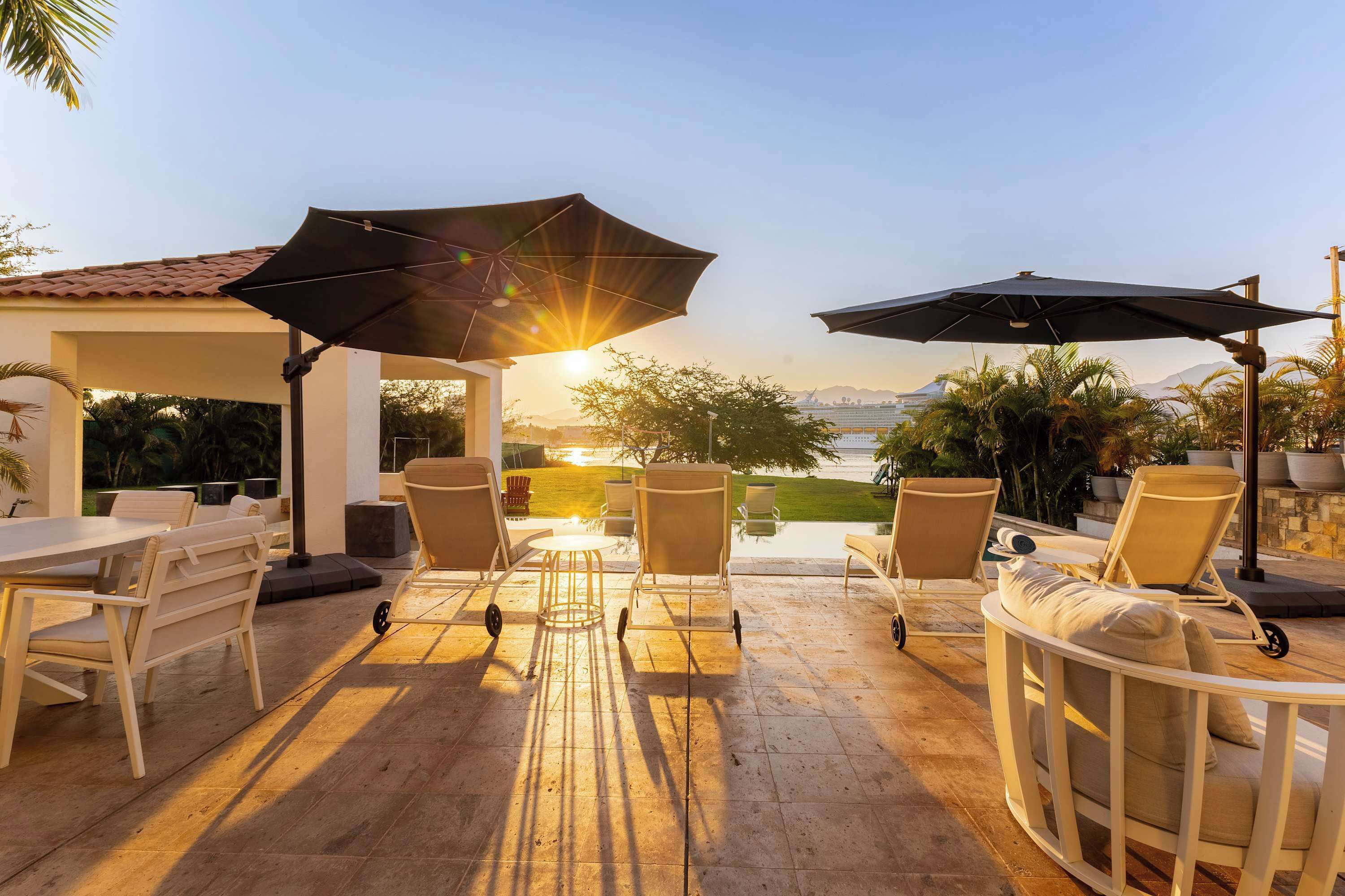 Une terrasse extérieure avec une table, des chaises et des parasols, offrant une vue sur un plan d’eau et des montagnes.
