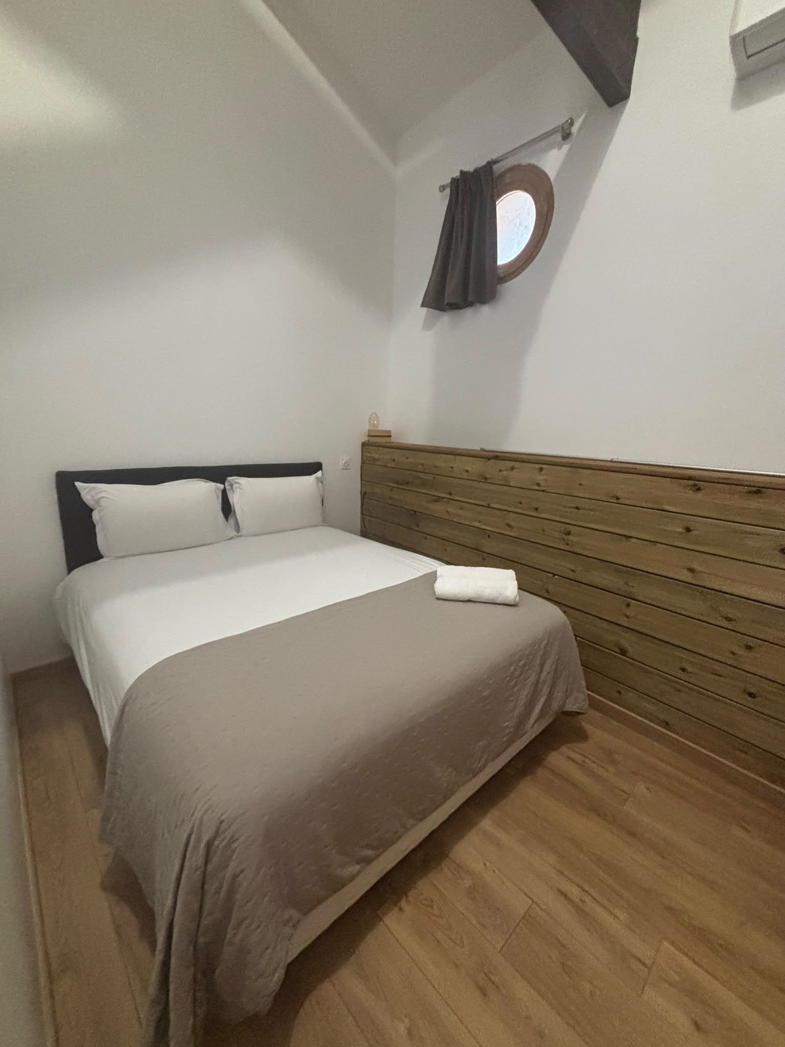Una cama individual con cabecera de madera, almohada blanca y colcha marrón.