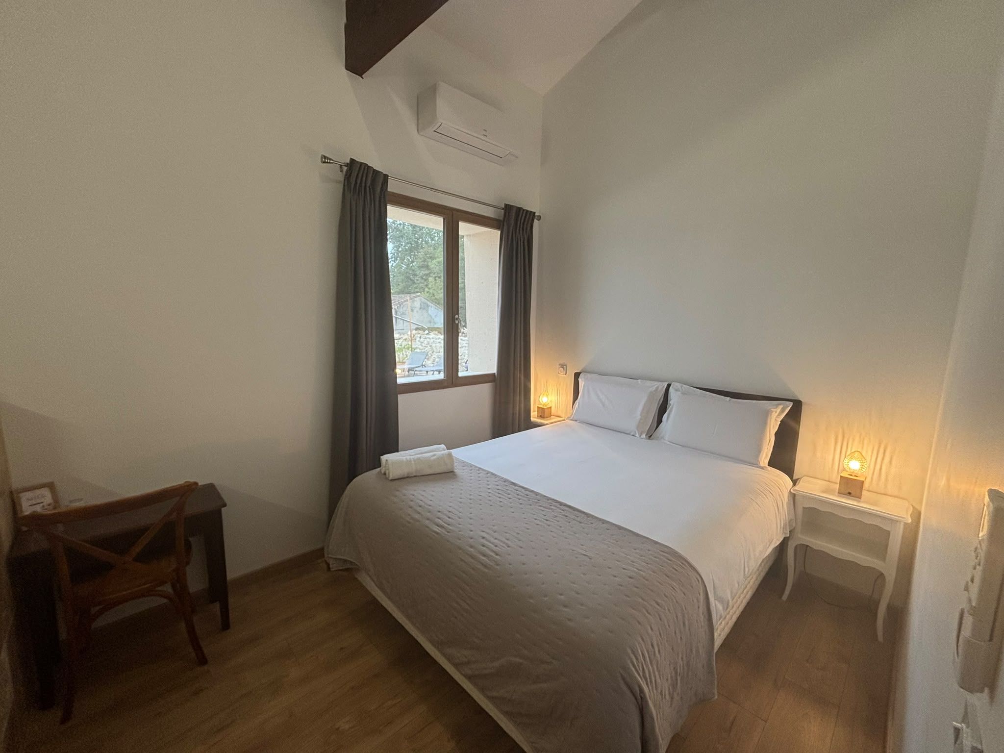 A bedroom with a bed, a desk, and a window with curtains.