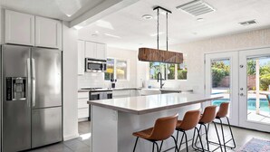 Une cuisine moderne dotée d’un îlot central, d’appareils électroménagers en acier inoxydable et offrant une vue sur une piscine.