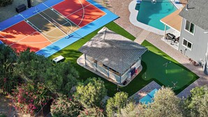 Un jardin avec un terrain de basket, une piscine, une terrasse couverte et un petit kiosque.