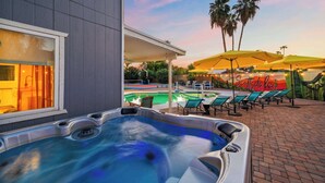 Un bain à remous et un espace extérieur aménagé avec des sièges, une piscine et des palmiers.