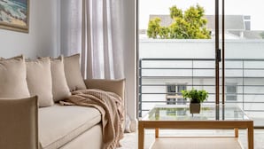A living room with a beige sofa, a glass coffee table, and a view of greenery through a sliding glass door. - Cozy Corner Apartment (Cape Town)