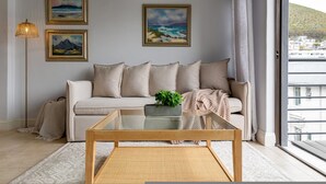 A living room with a sofa, a glass coffee table, and a floor lamp. There are three framed paintings on the wall. - Cozy Corner Apartment (Cape Town)