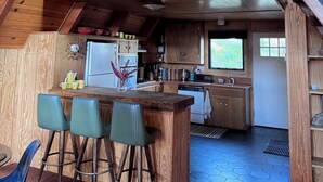 A rustic cabin with a loft bedroom, a kitchen with wooden cabinets, and a dining area with bar stools. - A-Frame with Carousel Fireplace - escape to the mountains and get out in natu... (Running  Springs)