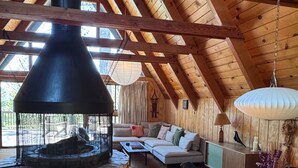 A cozy living room with a stone fireplace, wooden beams, a sofa, and a dining area with chairs. - A-Frame with Carousel Fireplace - escape to the mountains and get out in natu... (Running  Springs)