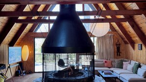 A cozy room with a stone fireplace, wooden beams, a sofa, and a painting on the wall. - A-Frame with Carousel Fireplace - escape to the mountains and get out in natu... (Running  Springs)