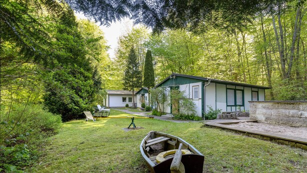 Una cabaña con un bote pequeño en el patio, rodeada de un bosque denso.