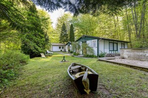 A cabin with a small boat in the yard, surrounded by dense forest.
