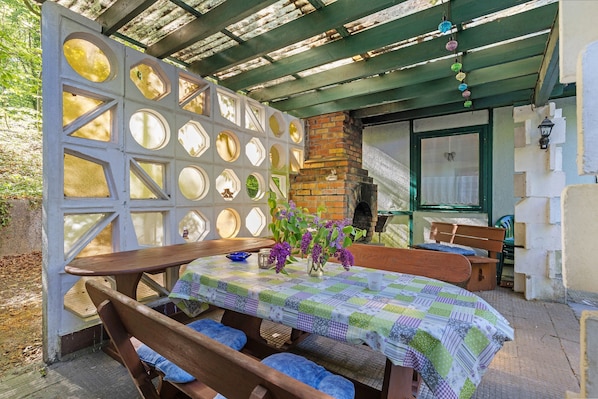 An outdoor patio with a wooden table and benches, a brick fireplace, and a decorative wall with circular cutouts.