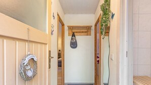 Un pasillo con una puerta de madera, un adorno de bienvenida, un bolso colgado y un espejo en la pared.