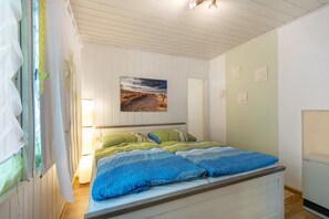 Une chambre à coucher avec un lit, une fenêtre avec des rideaux, un tableau accroché au mur et une table de chevet.