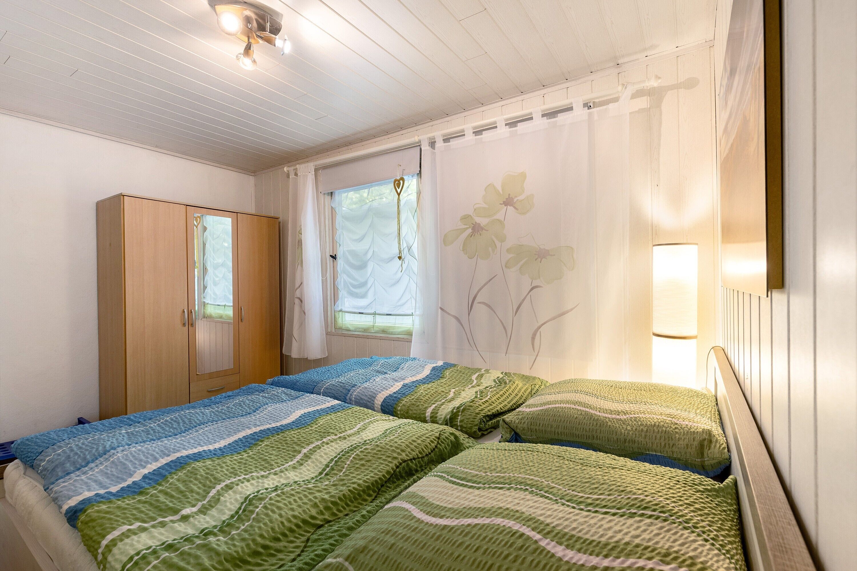 Ein Schlafzimmer mit Bett, Kleiderschrank, einem Fenster mit Vorhängen und einer Wandleuchte.