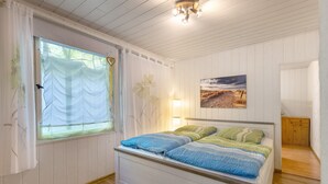 Un dormitori amb llit, finestra amb cortines, una làmpada i un quadre a la paret.
