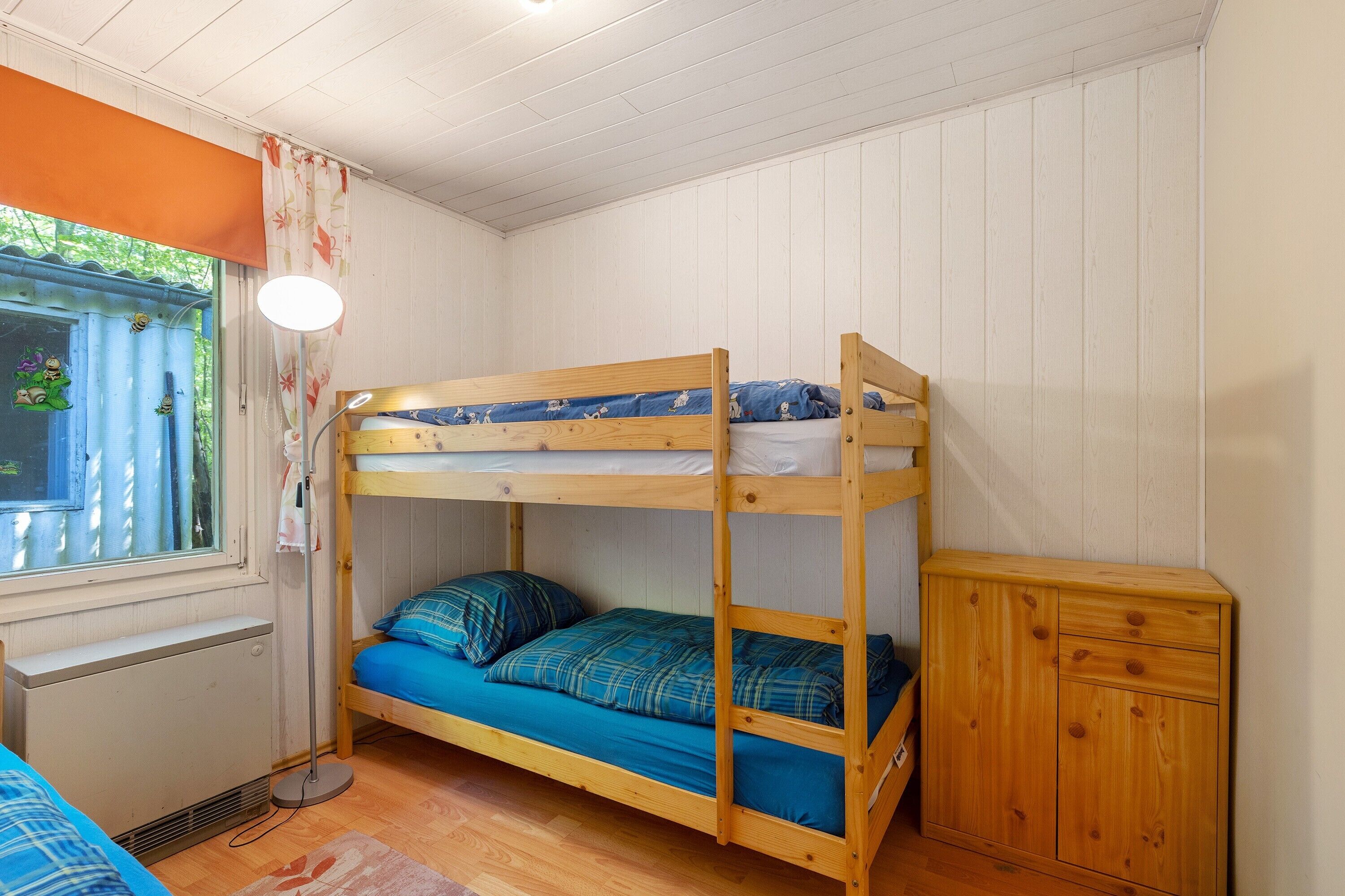 Un lit superposé avec un lit en bas, une table de chevet, une lampe et une fenêtre avec des rideaux.
