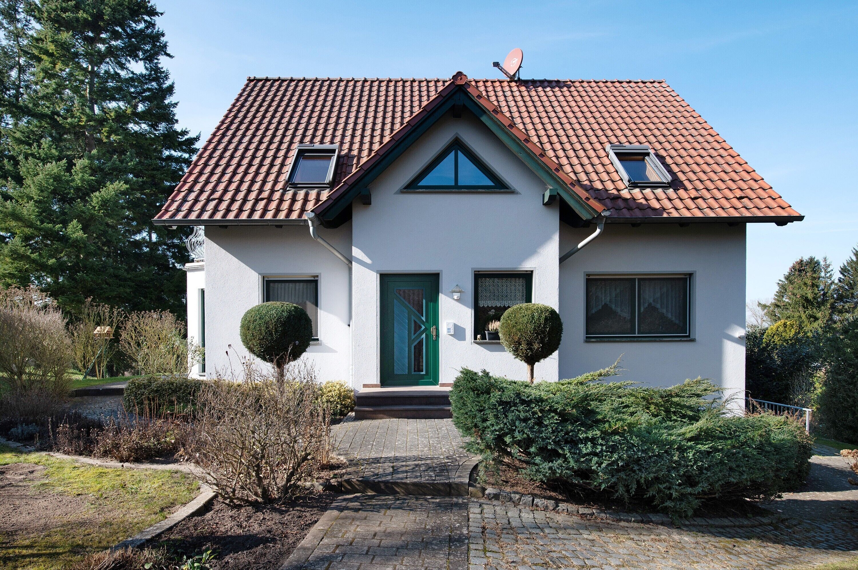 Ein zweistöckiges Haus mit rotem Ziegeldach, einer grünen Tür und zwei kleinen Fenstern im Obergeschoss.
