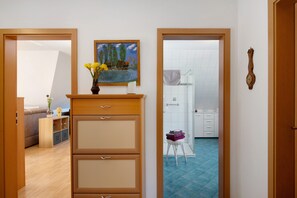 A room with a wooden cabinet, a painting, a vase with flowers, and a glimpse of a bathroom with a shower and tiled floor.