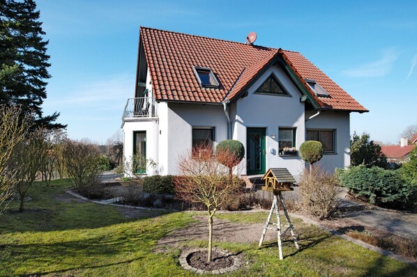 Une maison à deux étages, avec un toit recouvert de tuiles rouges, un petit balcon et un jardin bien entretenu.