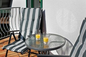 A round glass table with two glasses of orange juice, a striped chair, and a view of a building.