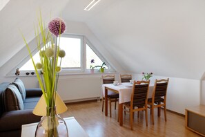 Un coin repas avec une table et des chaises, un vase avec des fleurs, une fenêtre donnant sur un beau paysage et un radiateur.