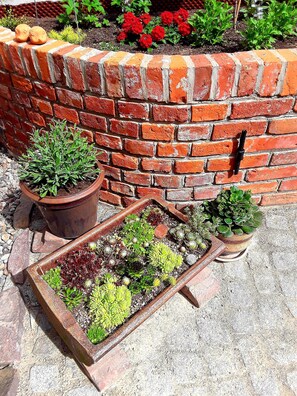 Un mur de briques agrémenté de plantes en pot et d’une jardinière en bois contenant des plantes succulentes.