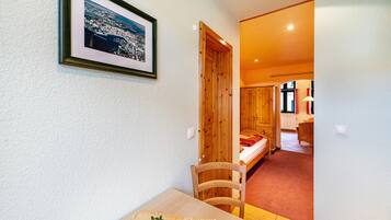 Ein Zimmer mit Holztür, einem Bett, einem kleinen Tisch mit einer Vase und einem gerahmten Bild an der Wand.